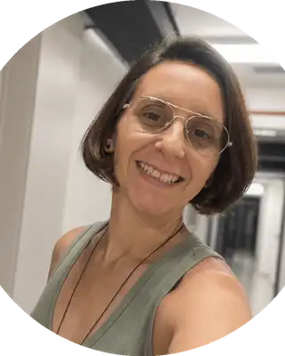 Retrato de Ju Panissa, mulher branca de cabelos castanhos curtos, usando óculos de armação fina e blusa verde, sorrindo.