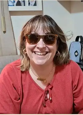 Retrato de Luciane Molina, mulher branca de cabelos castanhos na altura dos ombros, usando óculos escuros e blusa vermelha, sorrindo.