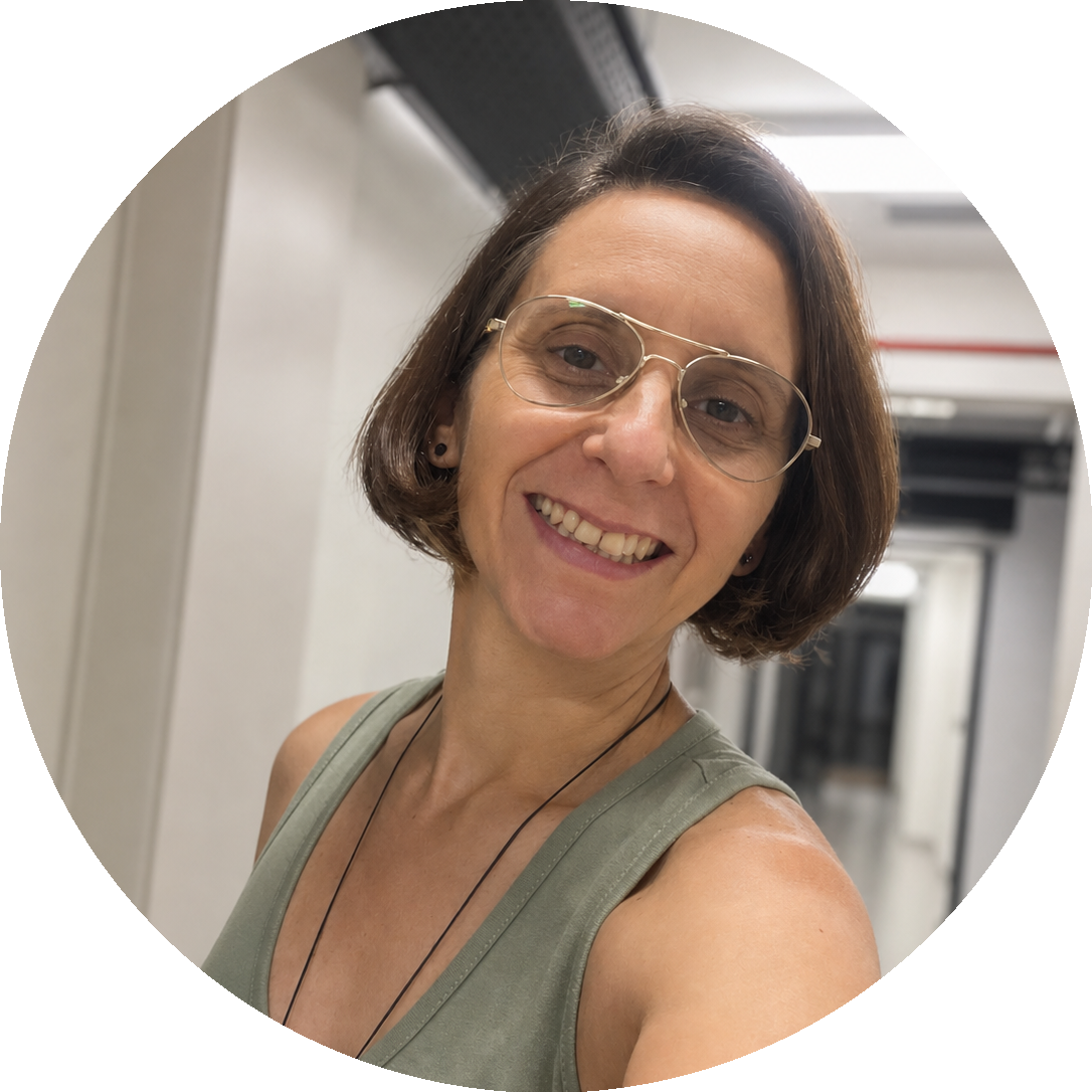 Retrato de Ju Panissa, mulher branca de cabelos castanhos curtos, usando óculos de armação fina e blusa verde, sorrindo.
