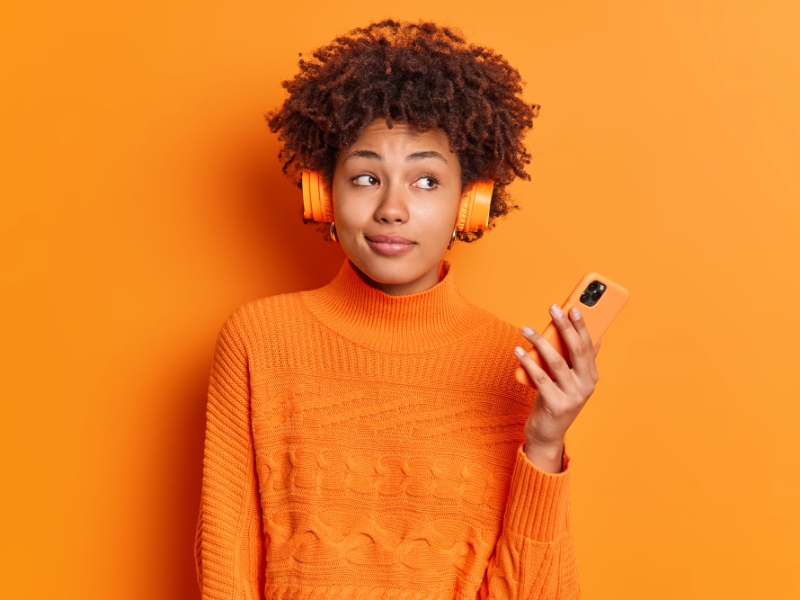 Acessibilidade Digital - Jovem mulher com fones de ouvido e um celular na mão, olhando para o lado.