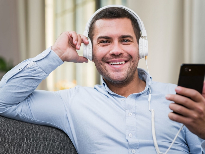 Audiodescritor - Um homem sorrindo, usando fones de ouvido e segurando um smartphone.