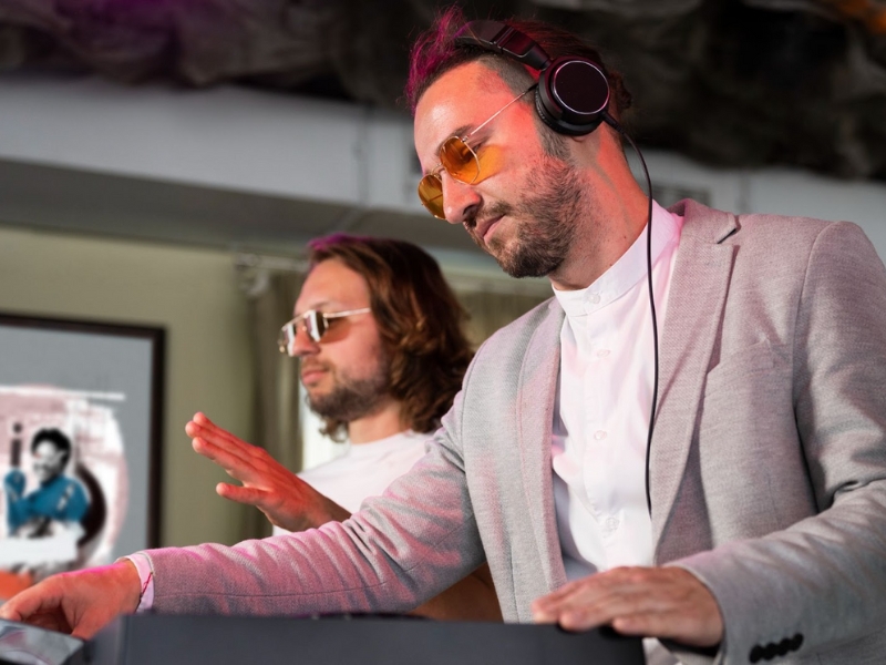 Audiodescrição em Eventos - Esta imagem é uma fotografia de dois homens trabalhando em um evento, com foco no homem em primeiro plano que está usando fones de ouvido.