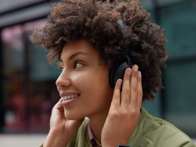 Esta imagem é um close-up em fotografia de uma jovem mulher sorrindo e usando fones de ouvido. - Como Fazer Audiodescrição